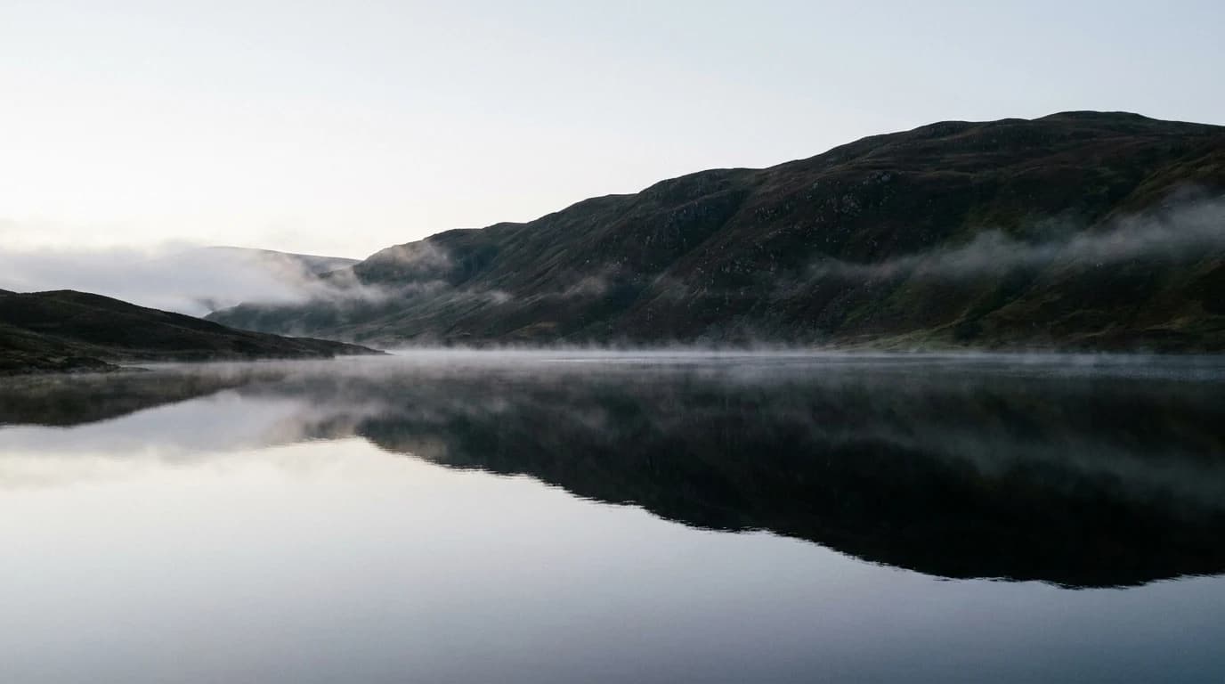 A misty Scottish Highland loch at early morning, perfectly still.