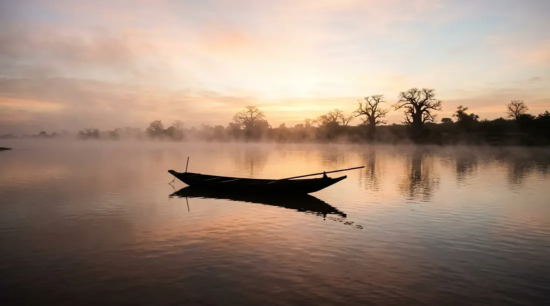 The Niger River at dawn in Mali, mist rising over still water.